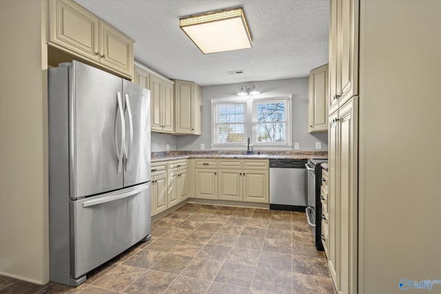 kitchen featuring cream cabinets, stainless steel appliances, a textured ceiling, and sink