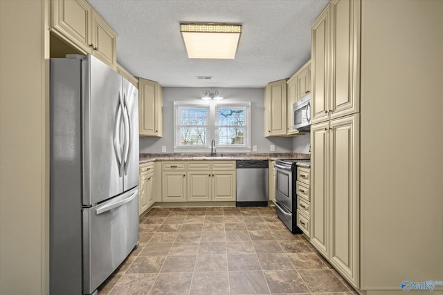 kitchen featuring sink, cream cabinets, a textured ceiling, and appliances with stainless steel finishes