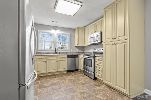 kitchen with sink, a textured ceiling, appliances with stainless steel finishes, and cream cabinets