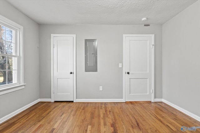 empty room with a textured ceiling, electric panel, and light hardwood / wood-style flooring