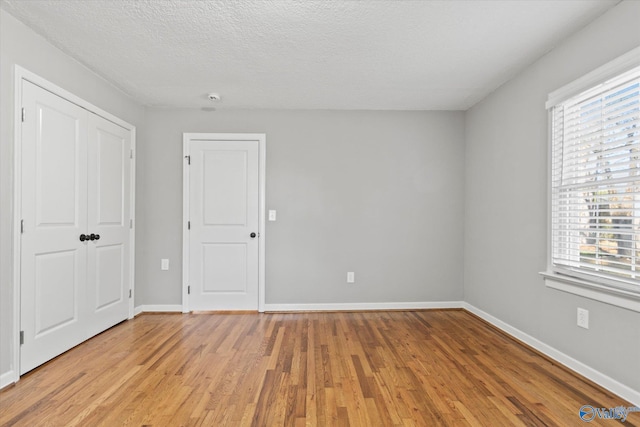 unfurnished room with a textured ceiling, a wealth of natural light, and light hardwood / wood-style flooring