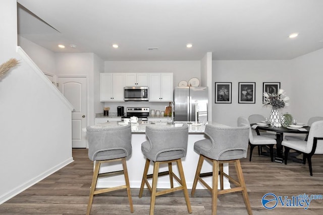 kitchen featuring appliances with stainless steel finishes, white cabinets, a breakfast bar, dark wood-style floors, and a kitchen island with sink