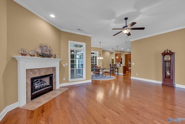 unfurnished living room featuring ceiling fan with notable chandelier, a fireplace, ornamental molding, and light hardwood / wood-style flooring