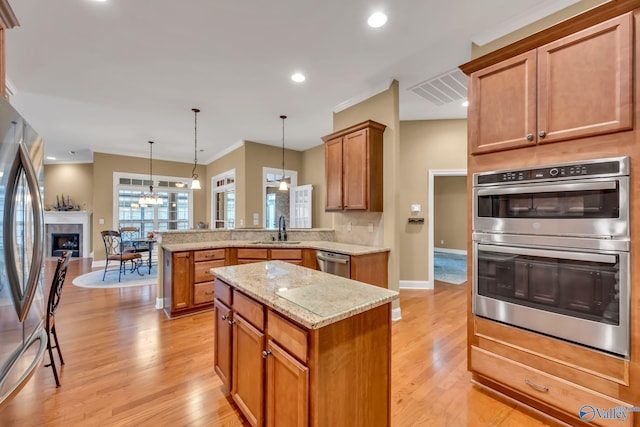 kitchen with appliances with stainless steel finishes, kitchen peninsula, light wood-type flooring, and pendant lighting