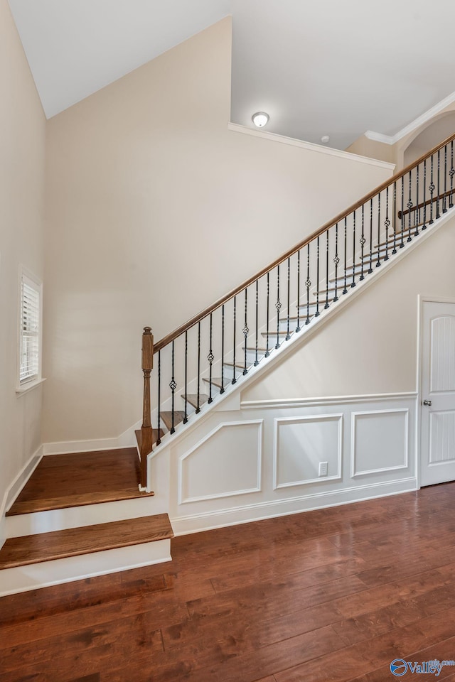 staircase with wood finished floors and high vaulted ceiling