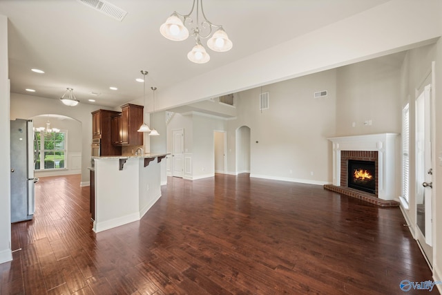 unfurnished living room featuring arched walkways, visible vents, a brick fireplace, and a chandelier