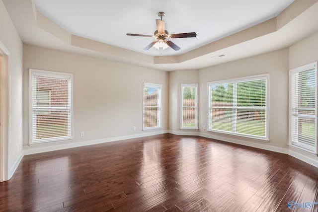 empty room with baseboards, a ceiling fan, dark wood-style flooring, and a tray ceiling