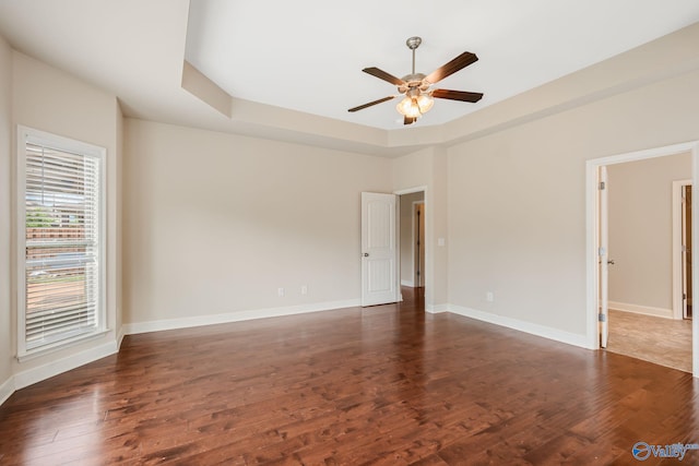 spare room featuring a ceiling fan, baseboards, a tray ceiling, and dark wood-type flooring