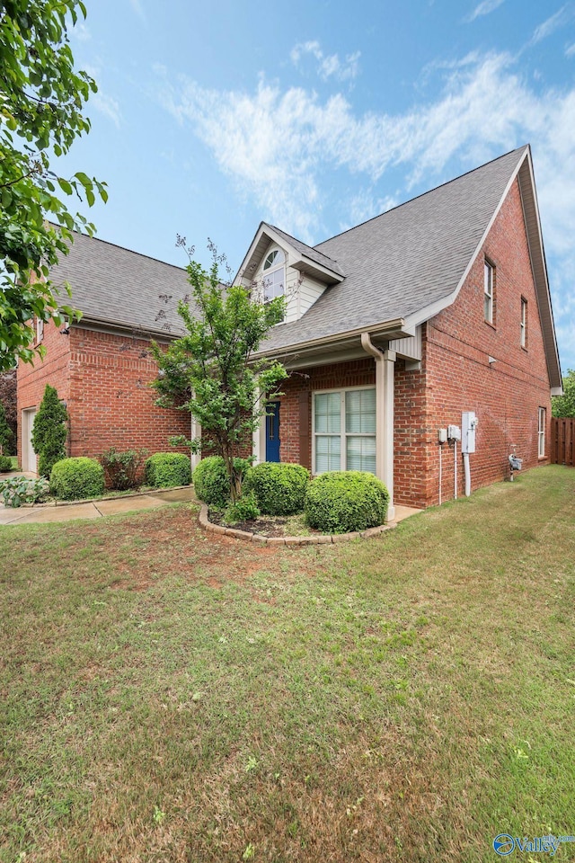 view of front of property featuring brick siding, an attached garage, a front yard, and roof with shingles