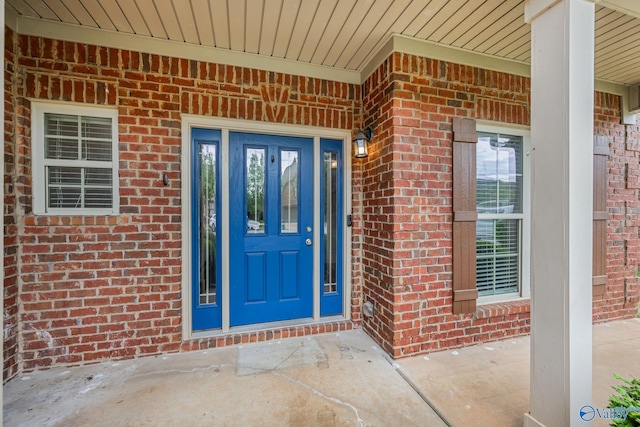view of exterior entry featuring covered porch and brick siding