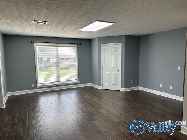 empty room featuring dark wood-type flooring, a textured ceiling, and baseboards