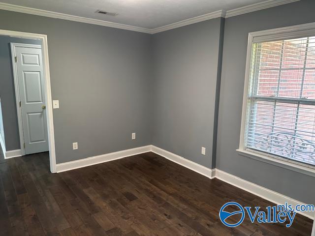 empty room with ornamental molding, dark wood-style flooring, visible vents, and baseboards