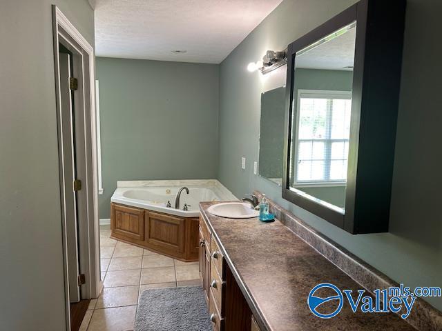 full bathroom with a garden tub, tile patterned flooring, a textured ceiling, and vanity