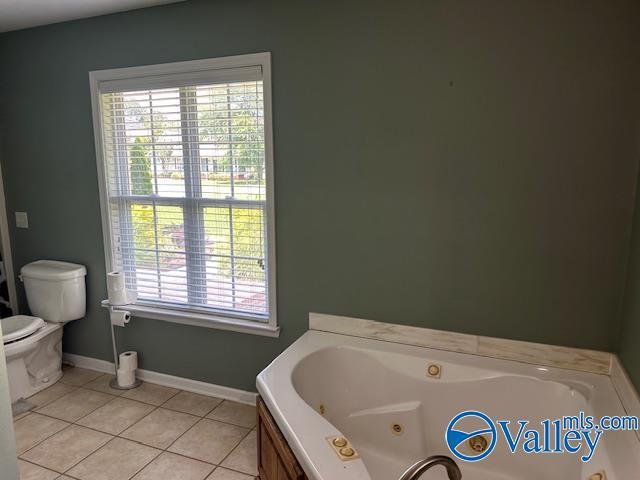 bathroom with tile patterned flooring, baseboards, toilet, and a whirlpool tub