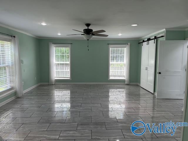 empty room featuring a ceiling fan, crown molding, baseboards, and a barn door