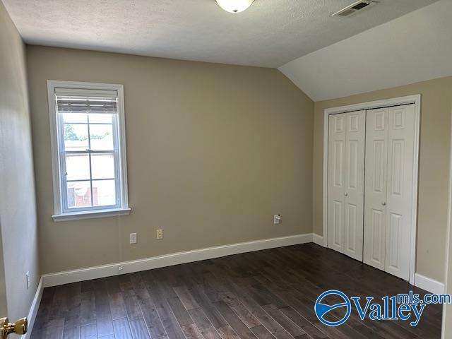 unfurnished bedroom featuring lofted ceiling, visible vents, dark wood-type flooring, a textured ceiling, and baseboards