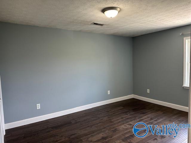 unfurnished room with a textured ceiling, dark wood-style flooring, visible vents, and baseboards