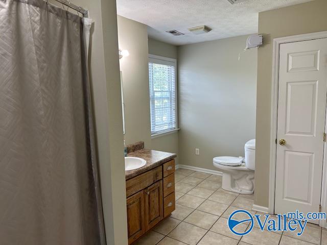 full bath with toilet, vanity, a textured ceiling, tile patterned flooring, and baseboards