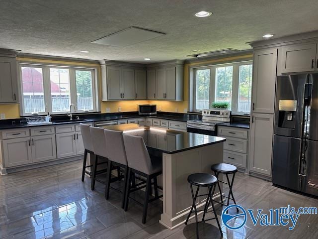 kitchen featuring a breakfast bar, stainless steel appliances, dark countertops, gray cabinets, and a kitchen island