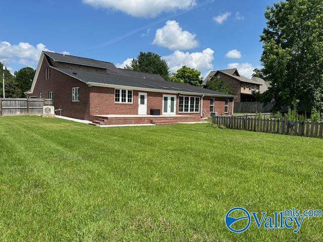 rear view of property with a yard, brick siding, and fence