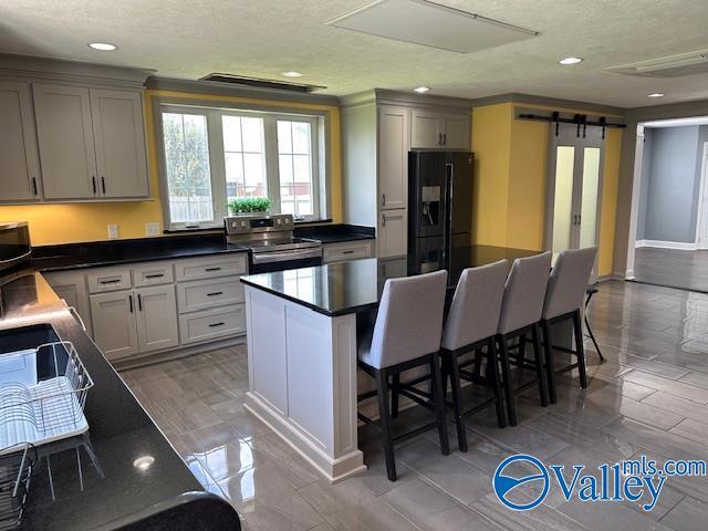 kitchen featuring a breakfast bar, stainless steel electric range oven, dark countertops, a barn door, and black fridge