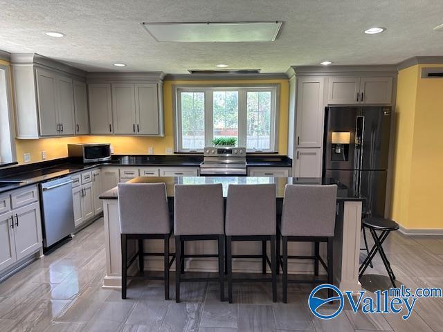 kitchen featuring a kitchen breakfast bar, appliances with stainless steel finishes, dark countertops, and gray cabinetry