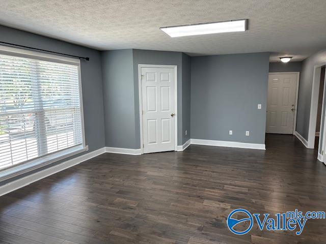 empty room with dark wood-type flooring, a textured ceiling, and baseboards