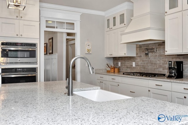 kitchen with stainless steel appliances, premium range hood, light stone countertops, and white cabinets