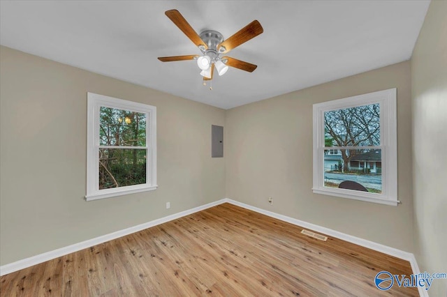 empty room with plenty of natural light, wood finished floors, electric panel, and baseboards