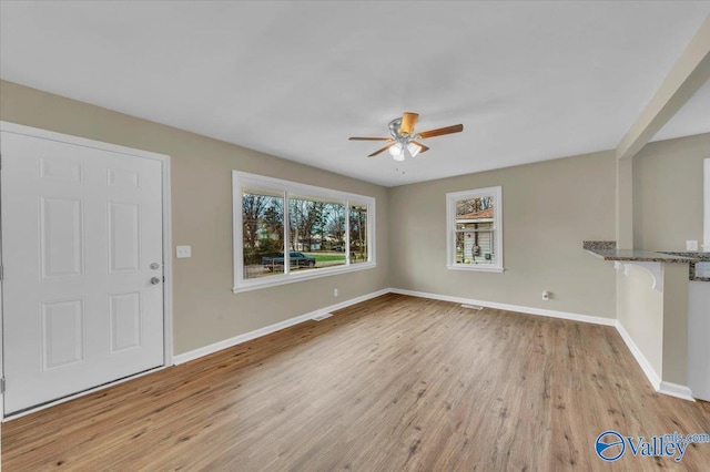 unfurnished living room with ceiling fan, light wood-style flooring, and baseboards