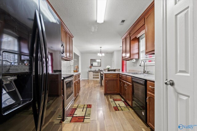 kitchen with black appliances, decorative light fixtures, sink, a chandelier, and light hardwood / wood-style flooring