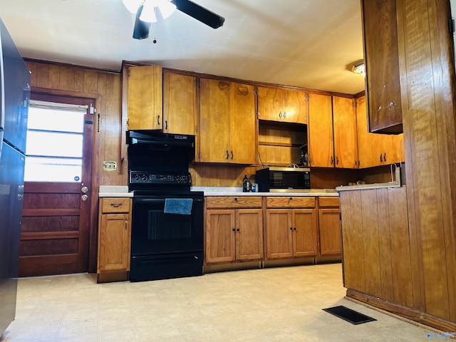 kitchen featuring ventilation hood, black range with electric stovetop, ceiling fan, and wood walls