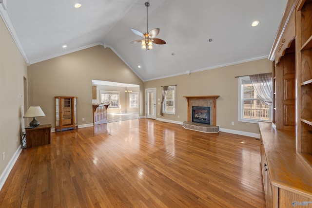 unfurnished living room with high vaulted ceiling, ornamental molding, a tile fireplace, hardwood / wood-style flooring, and ceiling fan