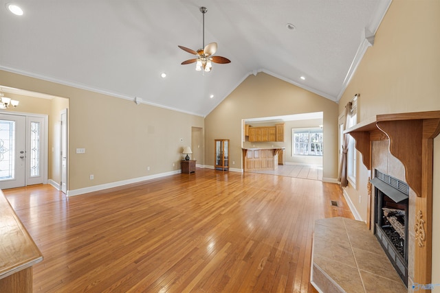 unfurnished living room featuring light hardwood / wood-style flooring, high vaulted ceiling, a fireplace, ornamental molding, and ceiling fan with notable chandelier