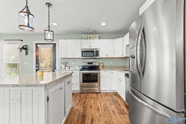 kitchen with white cabinetry, light stone countertops, appliances with stainless steel finishes, and wood finished floors