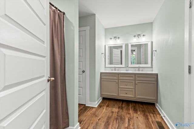 full bathroom with double vanity, baseboards, a sink, and wood finished floors