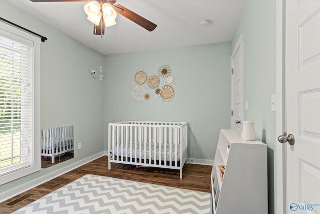 bedroom featuring a ceiling fan, visible vents, a nursery area, wood finished floors, and baseboards