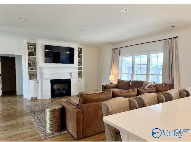 living room featuring crown molding, light wood-style flooring, recessed lighting, and a fireplace