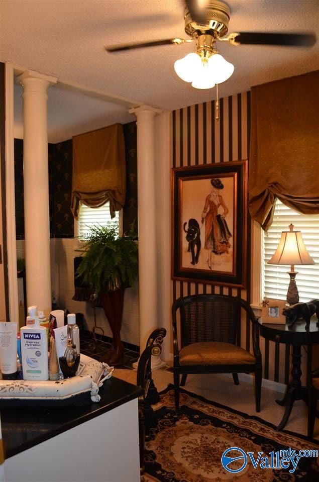 living area with wallpapered walls, decorative columns, and ceiling fan