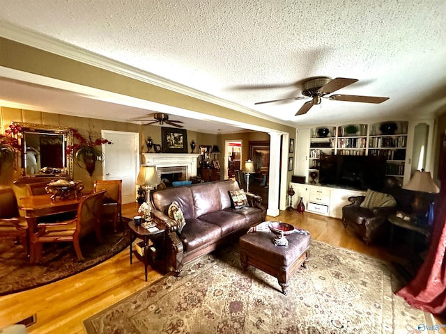 living area featuring ceiling fan, wood finished floors, a textured ceiling, crown molding, and a fireplace