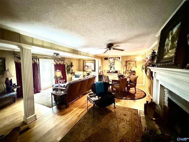 living area with a ceiling fan, ornamental molding, wood finished floors, a textured ceiling, and a fireplace