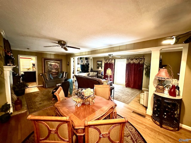 dining room featuring ceiling fan, a textured ceiling, wood finished floors, visible vents, and ornamental molding