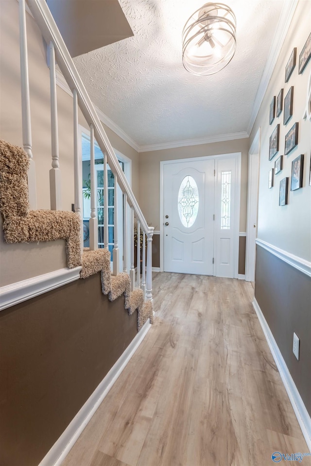 entryway featuring a textured ceiling, ornamental molding, stairway, and light wood-style floors