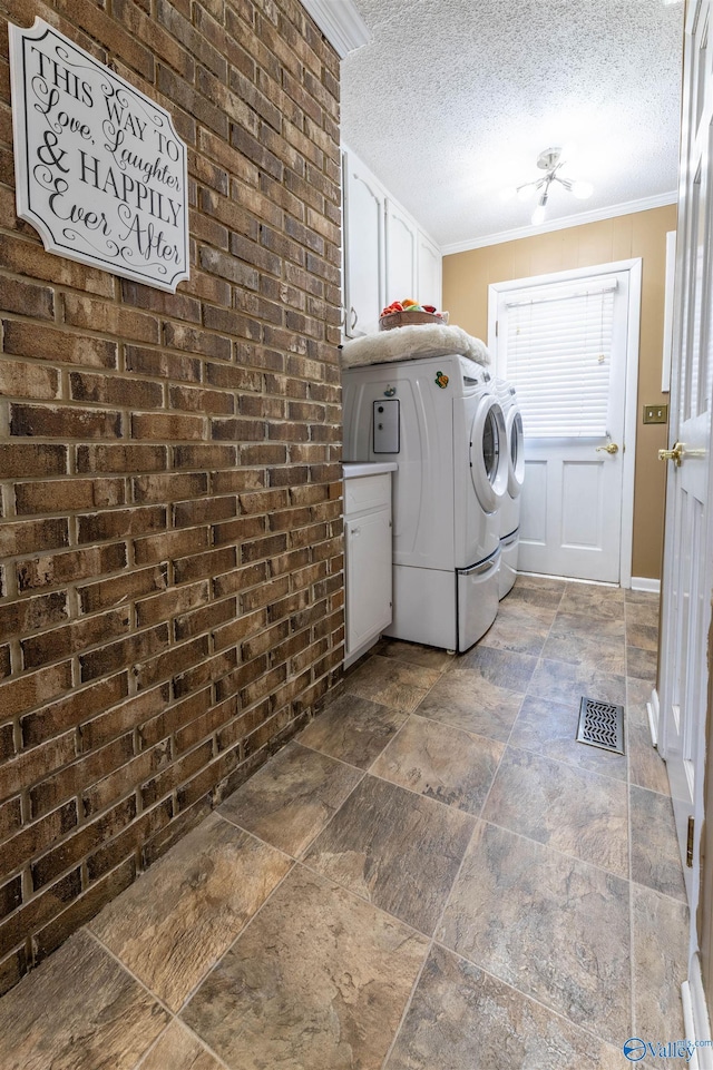 washroom with cabinet space, separate washer and dryer, a textured ceiling, stone tile floors, and ornamental molding