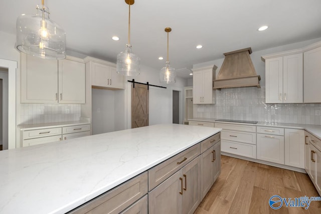 kitchen featuring decorative light fixtures, custom exhaust hood, light stone countertops, and a barn door