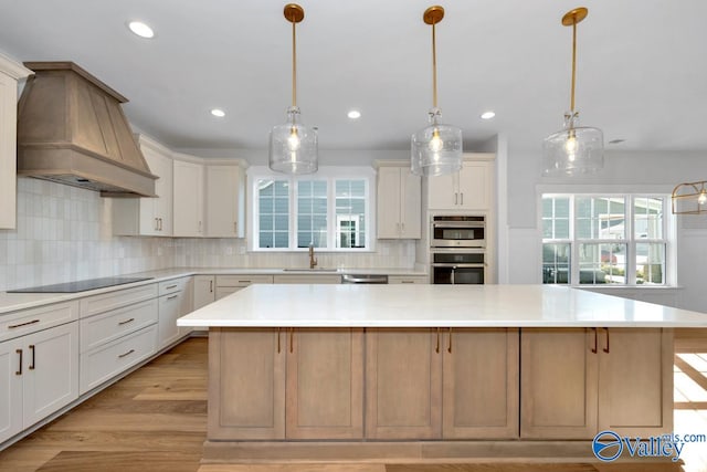 kitchen featuring premium range hood, sink, appliances with stainless steel finishes, pendant lighting, and a large island