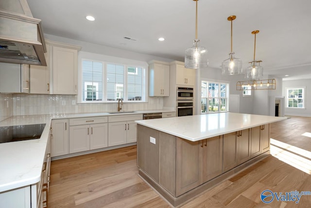 kitchen with a large island, sink, hanging light fixtures, and light hardwood / wood-style flooring