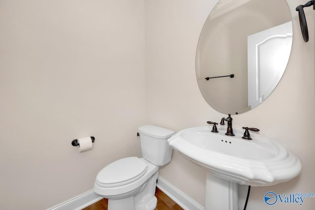 half bath with baseboards, a sink, and toilet