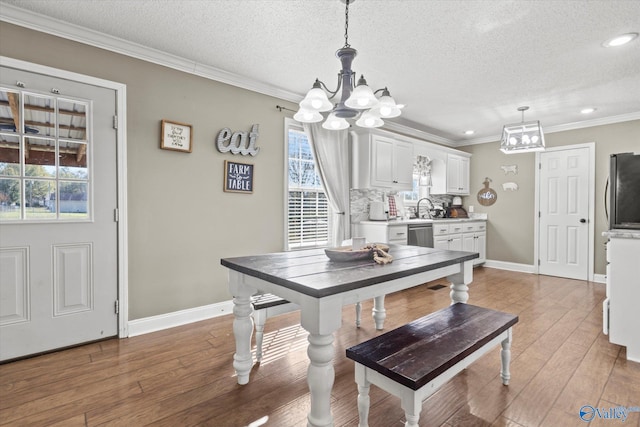 dining space with a textured ceiling, light hardwood / wood-style flooring, ornamental molding, and sink