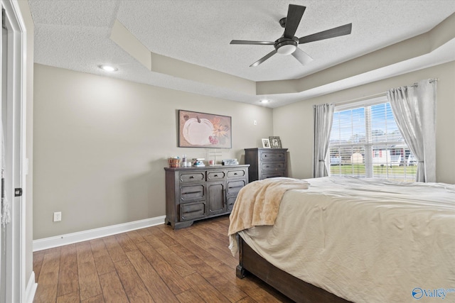 bedroom with hardwood / wood-style floors, a textured ceiling, a tray ceiling, and ceiling fan